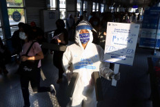 Wearing a hazmat suit, a member of a Transjakarta community holds up a sign with updated data on the number of COVID-19 cases in Jakarta to raise awareness on health protocols within the Harmoni bus shelter in Jakarta on July 17. JP/Dhoni Setiawan