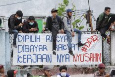 (Not) on the fence: Protesters sit on a wall above a banner during a peaceful demonstration on Thursday, October 7. 2020 in Harmoni, Central Jakarta. The banner gives voice to the protesters’ sense of public betrayal, pointing out that it is the people that elect and pay the salaries of lawmakers, only for them to “cause trouble”. JP/Wendra Ajistyatama