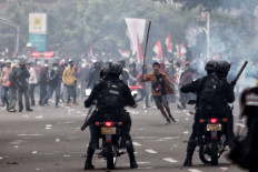 A protester runs toward police officers who stand guard on motorcycles during a clash in Jakarta on Oct. 13. A series of protests took place across the country following the House of Representatives’ decision to pass the jobs creation bill into law on Oct. 5. JP/Seto Wardhana