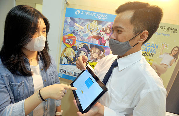 All about the youth: An employee (right) helps a customer conduct a digital transaction at the head office of J Trust Bank in Jakarta in this undated photo. J Trust Bank targets younger customers to increase its third-party funds.